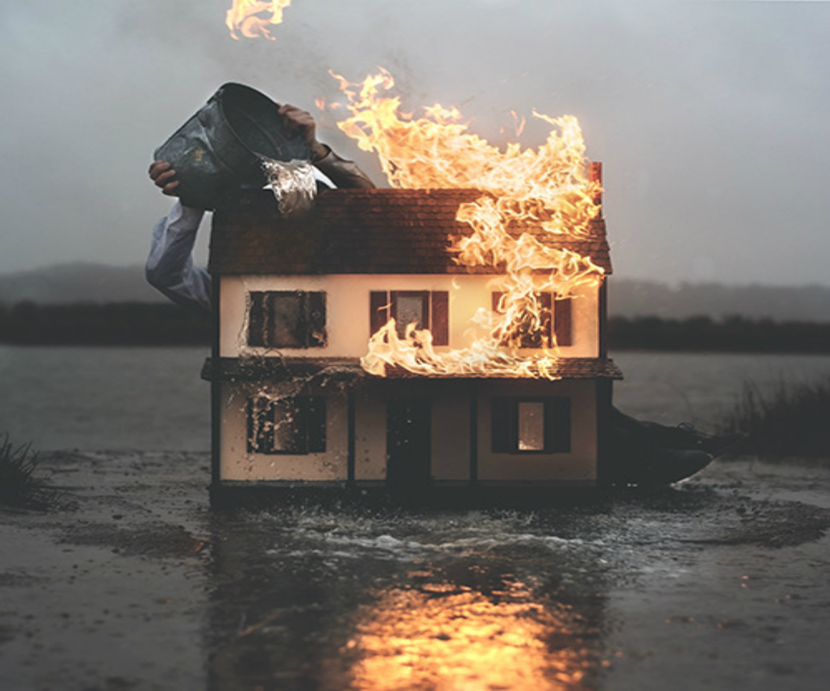 flaming miniature house with bucket of water being poured on it