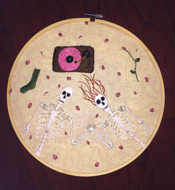Embroidered skeleton couple lying on the floor with rose pedals around them listening to a pink vinyl record