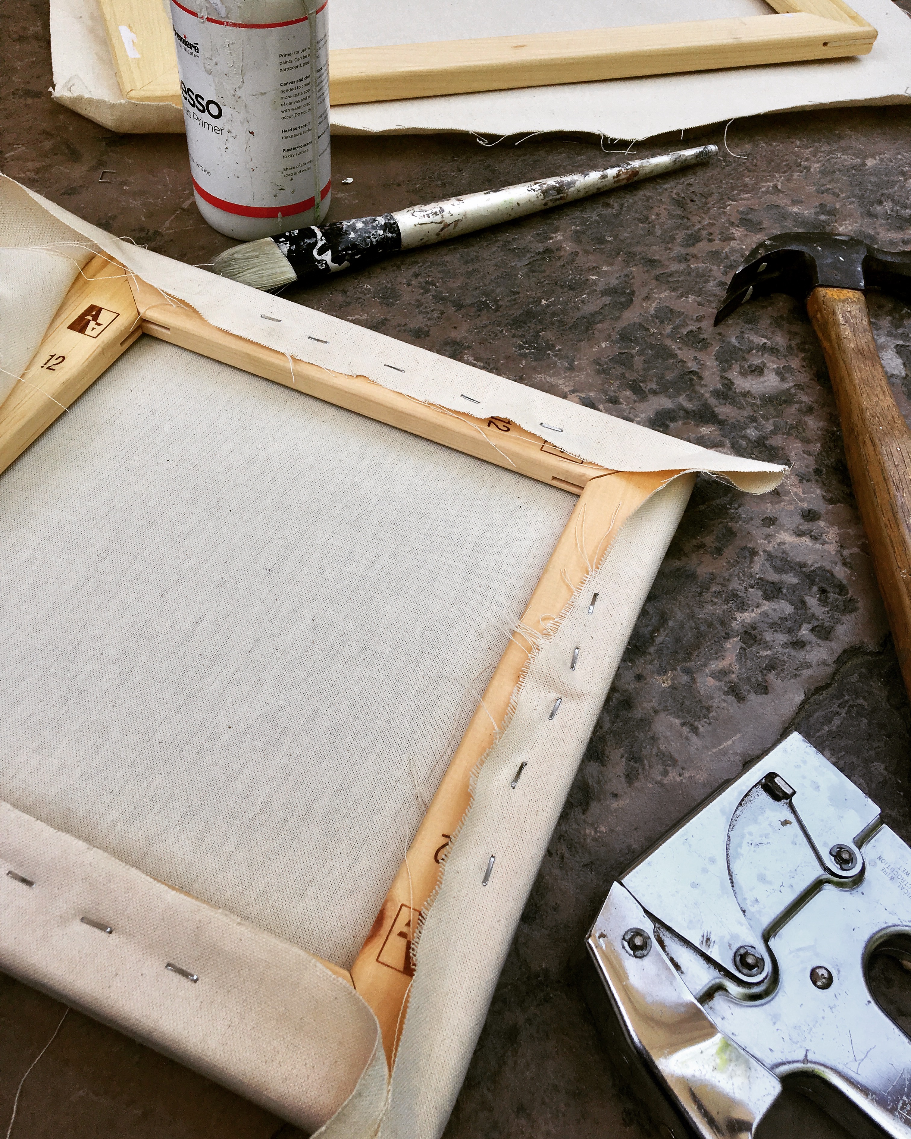 Back of canvas stretched across stretcher bars and tools (hammer, staple gun, gesso) used for stretching canvas