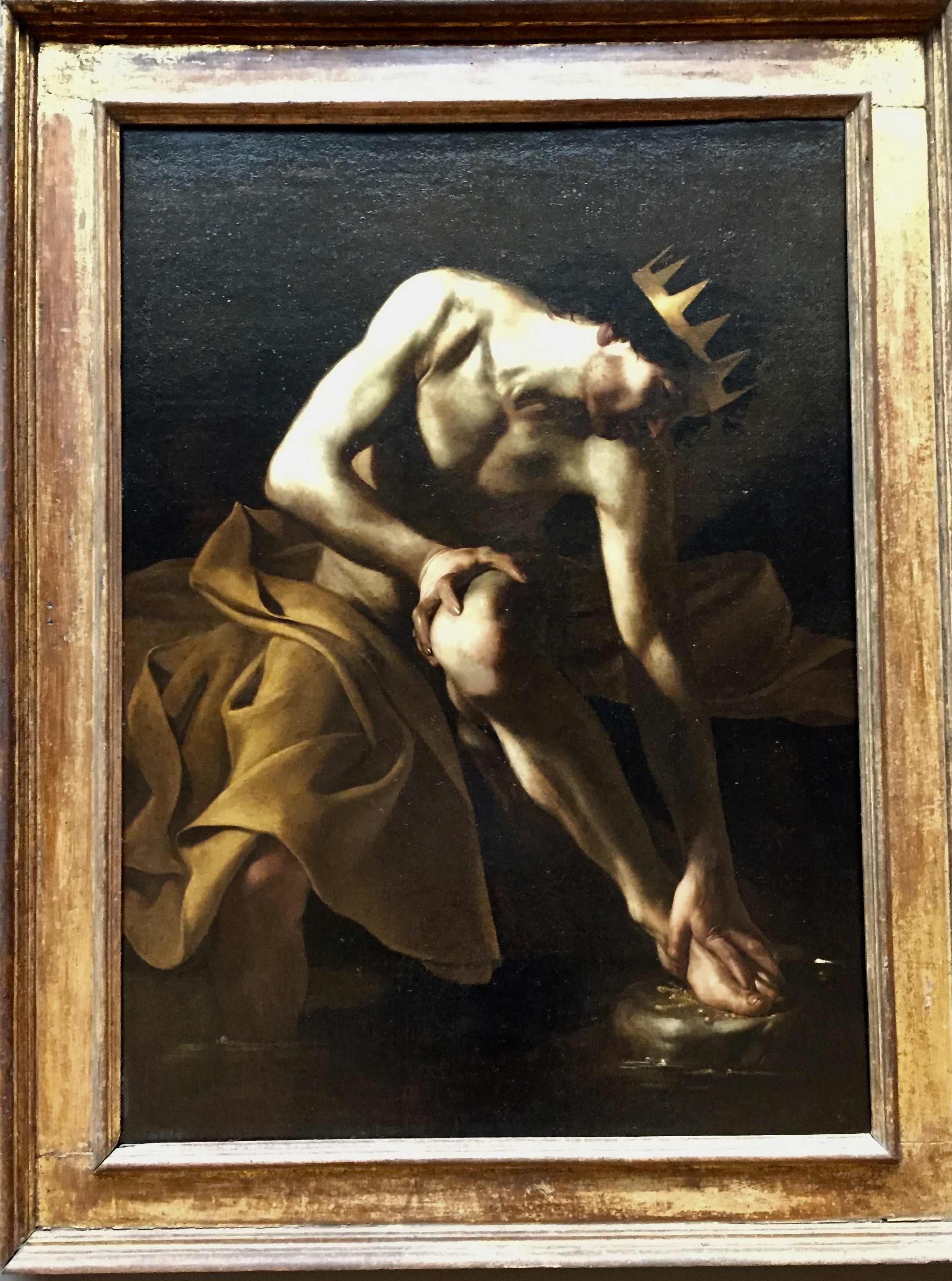 Man with crown and blanket washing feet in a river