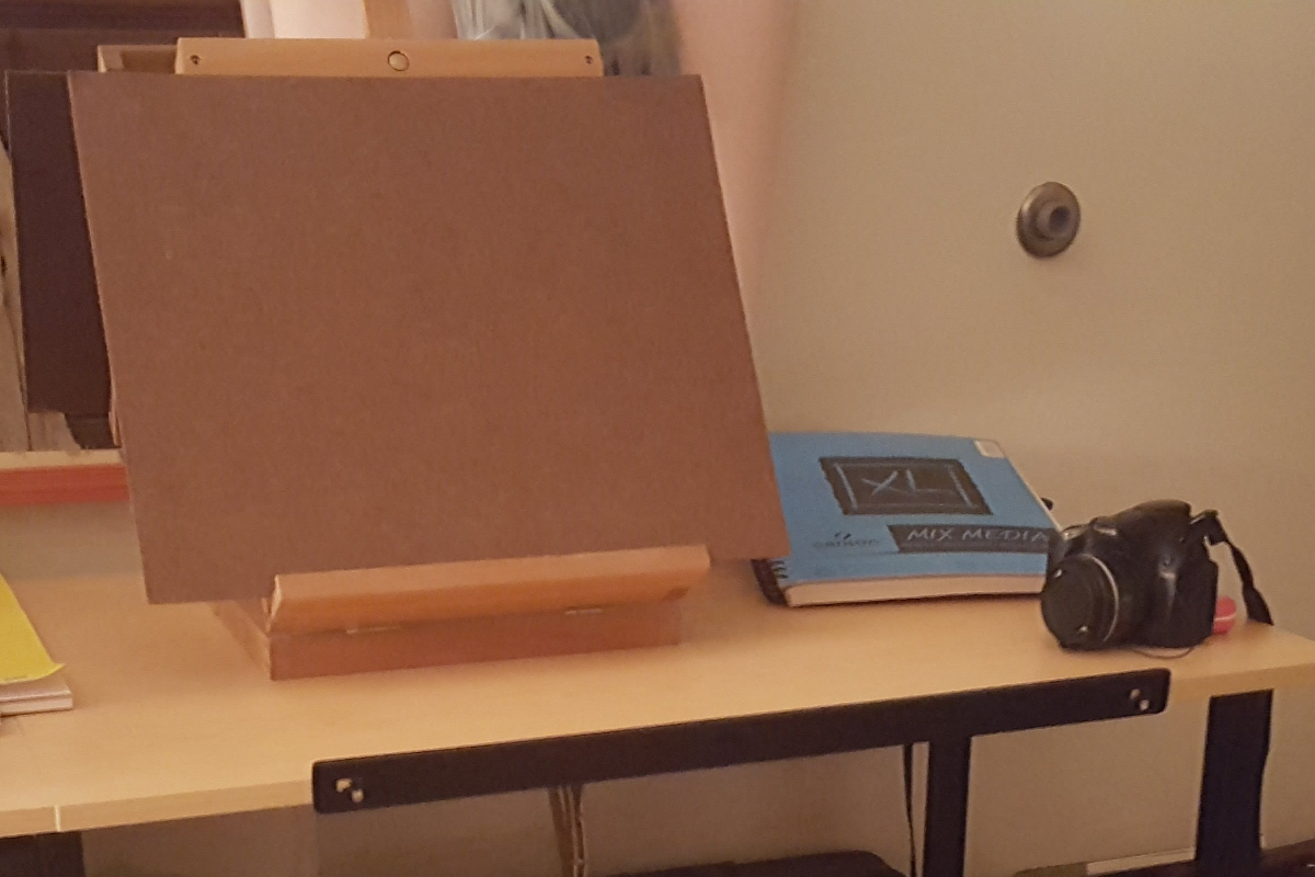 a desk with a camera, sketchbook, and table easel