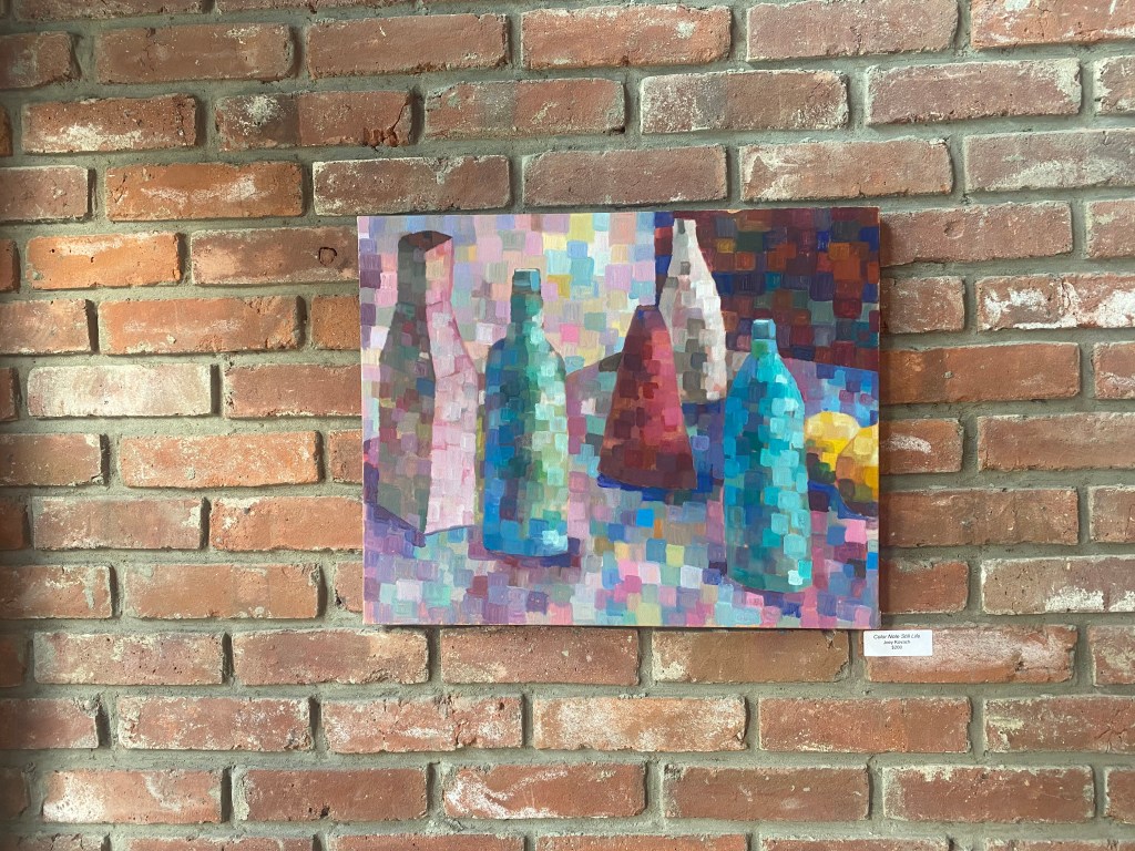 A painting of two green bottles, a red cone, a white carton and a white bottle, painted with a technique that emphasizes different color notes within the objects. The painting is hanging on a brick wall 