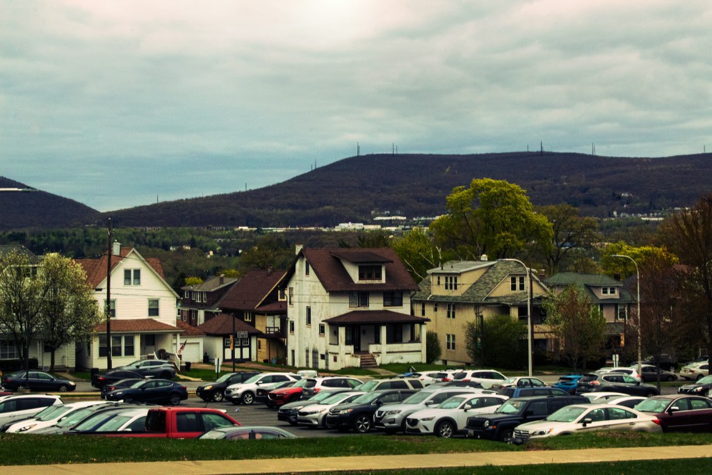 Landscape photo with cars in the foreground, houses in the middle ground, and mountains in the background