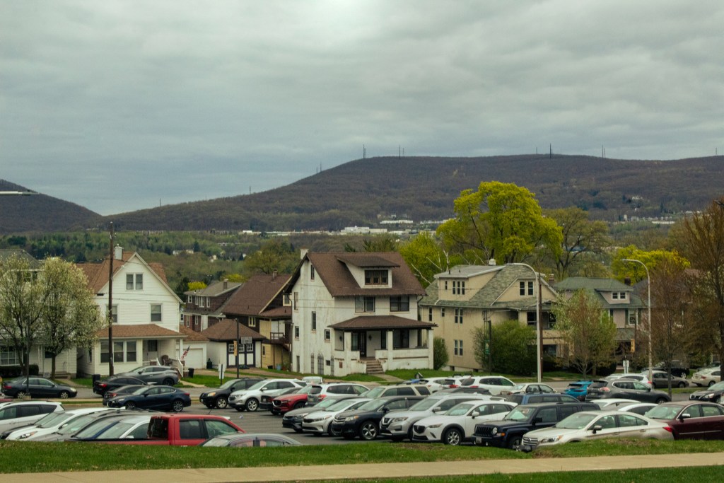 Landscape photo with cars in the foreground, houses in the middle ground, and mountains in the background