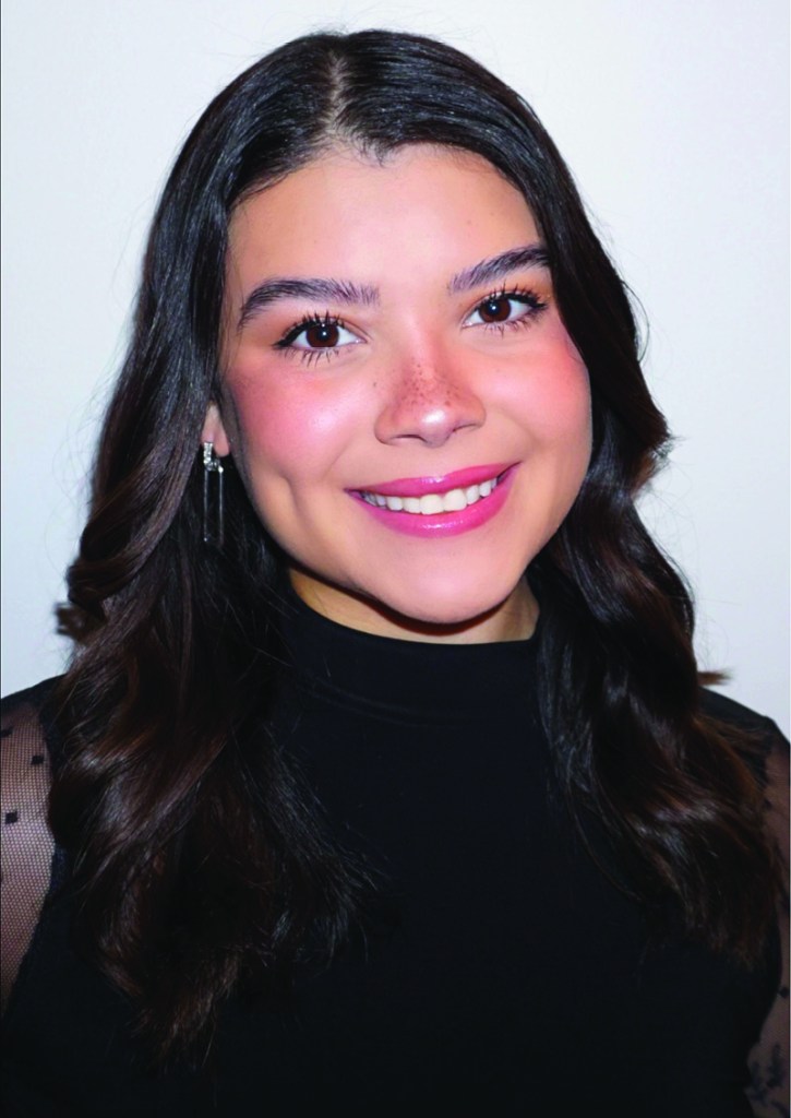 Portrait of a young woman with long dark hair, smiling warmly and wearing a black top.