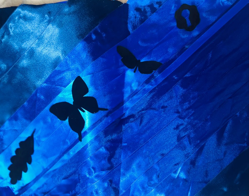 Phaedra Erzar ---“I was inspired by the images of the submerged insects in the “Beauty in the Imperfections” exhibit. I loved how bright the blues were, and I tried to portray that with the blue ribbon. I painted black over real images of insects to add to the piece as well.”